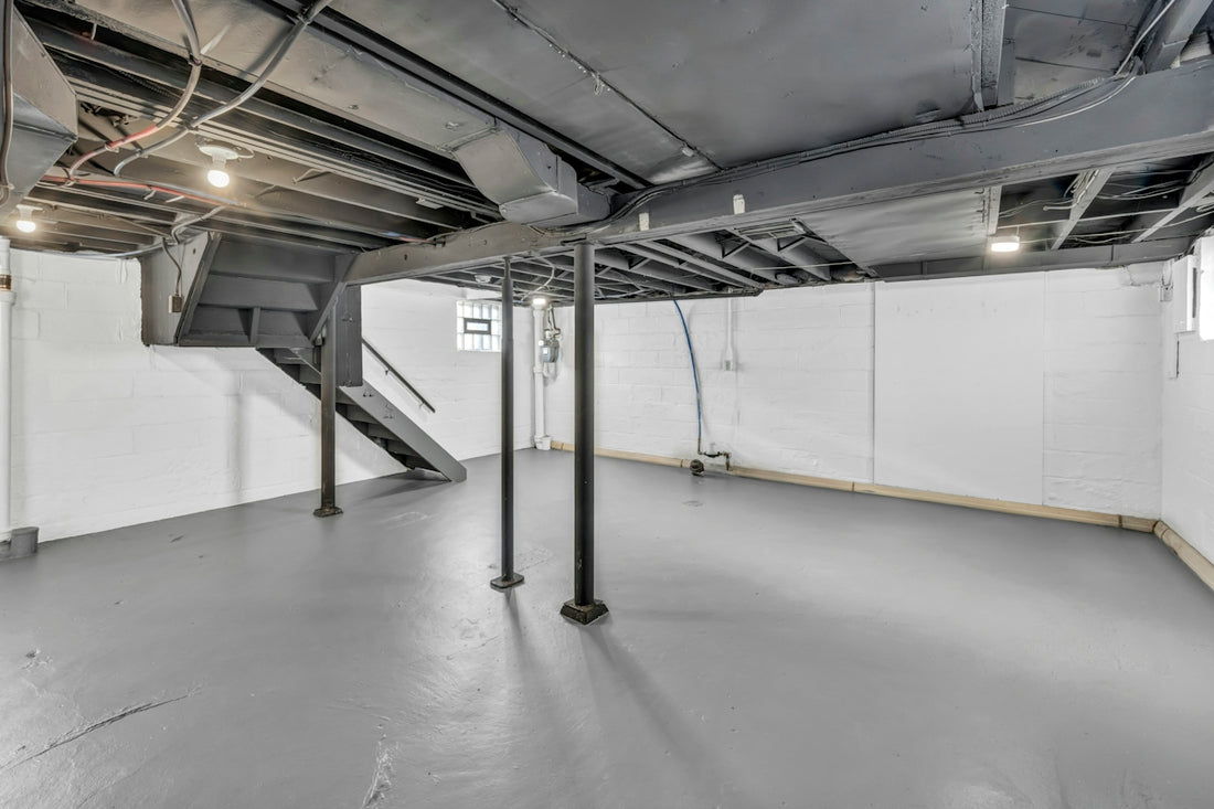 Spacious unfinished basement with exposed joists, support poles, and stairs