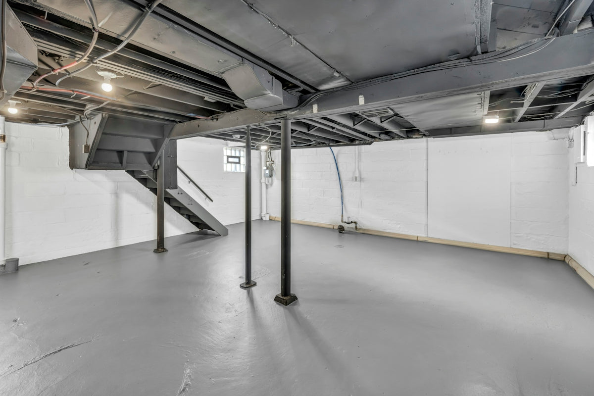 Spacious unfinished basement with exposed joists, support poles, and stairs